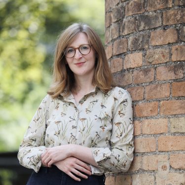 Anneke Lubkowitz lehnt an einer Mauer, leicht verschränkte Arme