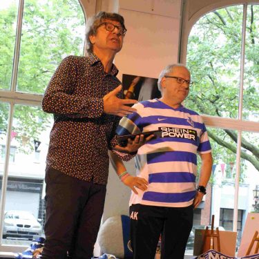 Auf der Bühne der Freundschaft steht Moderator Ralf Koss aka Kees Jaratz zusammen mit einem Fußballfan, der über besondere Erinnerungen an den Fußball in seinem Leben einen Text geschrieben hat.